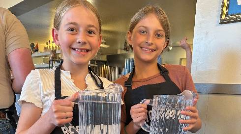 Two young volunteers in Bestowing the Basics aprons ready to serve at a community meal
