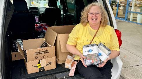 A Brighter Life Foundation volunteer holding prepackaged CoPow Foods meals beside a loaded van